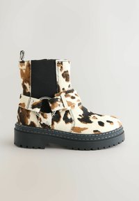Bocanci din piele pentru gleznă cu un design în imprimeu de vacă, având panouri elastice laterale negre, un accent cu inel argintiu și o talpă groasă neagră.