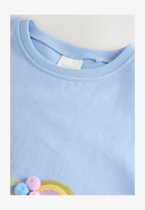 Light blue cotton t-shirt featuring a round neckline, with a colorful embroidered rainbow design and pom-pom accents at the hem.