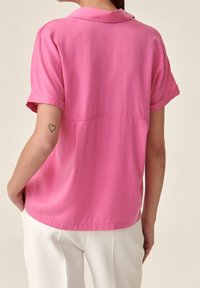 Kurzärmlige rosa Bluse mit klassischem Kragen und lockerer Passform, mit aufgeschlagenen Ärmeln und glattem Stoff.