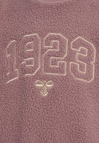 Fleece sweatshirt i mauve med hævede, broderede tal "1923" i guld. Har en blød, nubret tekstur og et lille bi-emblem nedenfor.