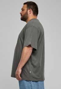 Kurzes, graues T-Shirt mit l�ässiger Passform, rundem Halsausschnitt und einem kleinen Logo-Detail am Saum. Weicher Stoff mit glatter Textur.