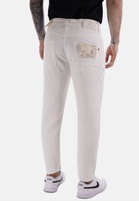 Pantaloni in denim bianco con taglio dritto, due tasche posteriori e una toppa etichetta, abbinati a sneakers bianche con uno swoosh nero.