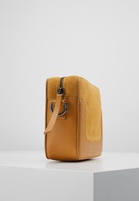 Żółta skórzana i zamszowa torba na ramię z zamkiem błyskawicznym u góry, płaskim designem i akcentem w postaci bocznego paska. Posiada teksturowany przedni panel oraz metalowe okucia.