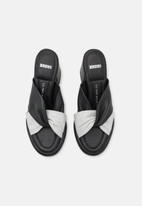 Black and white slip-on sandals featuring a twisted front design in smooth leather. Black soles with logo detail on the insole.