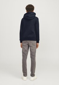 Sudadera azul marino con una capucha grande, combinada con jeans gris claros. Las zapatillas blancas completan el atuendo. La vista muestra la parte posterior de la ropa.