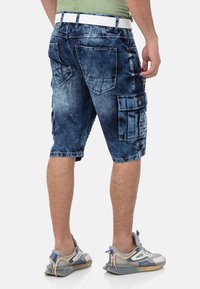 Denim-Cargo-Shorts in einer ausgeblichenen blauen Waschung, mit mehreren Taschen, geradem Schnitt und einem weißen Gürtel. Die Textur ist glatt mit leichter Abnutzung.