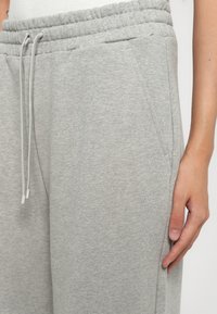 Nærbillede af en persons hånd, der hviler ved siden af afslappede, lysegrå sweatpants med elastisk talje og snøre.