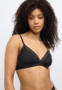 Must pitsiga kaunistatud pitsirinnahoidja, millel on sile kangas, kolmnurkse kujuga tassis ning elastsest ribast, millel on peen muster lisatud detaili jaoks.