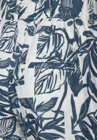 Látka s květinovým vzorem v námořnické modři a bílé barvě, obsahující listové motivy; zahrnuje švový kapsu a lehký, strukturovaný lněný materiál.