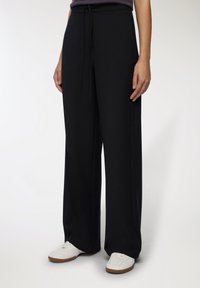 Czarne szerokie spodnie wykonane z miękkiego materiału, z elastycznym paskiem w talii i dwiema bocznymi kieszeniami. W zestawie z białymi sneakersami.