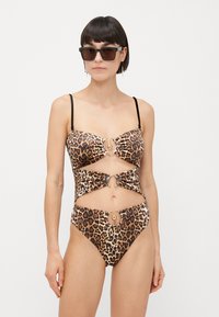 Bikini con stampa leopardata e dettagli dorati, caratterizzato da un design con ritaglio e spalline nere regolabili. Il tessuto ha una texture liscia e elastica.