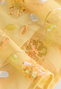 Tissu jaune transparent avec des motifs floraux brodés en sequins brillants orange, verts et bleus et fines tiges en fil.