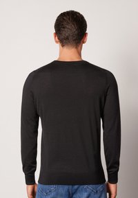 Svart långärmad tröja i ett mjukt stickat material, med rundad halsringning och ribbade ärmslut, buren av en person som står med ryggen vänd.