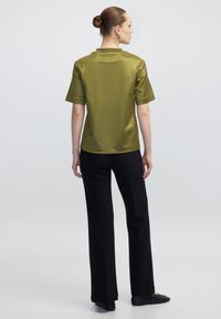 Olijf groene satijnen top met korte mouwen en een ronde hals, gecombineerd met zwarte broek. De gladde textuur en de ontspannen pasvorm versterken het ontwerp.
