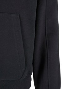 Primer plano de tela negra con un bolsillo rectangular cosido y puño acanalado, mostrando la textura y los detalles de costura en la manga de la prenda.