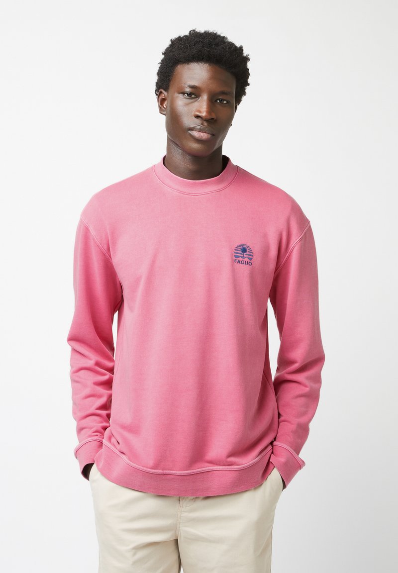 Sudadera rosa con escote redondo y mangas largas. Cuenta con un logo azul marino en el pecho. Está hecha de una tela suave con una textura lisa.