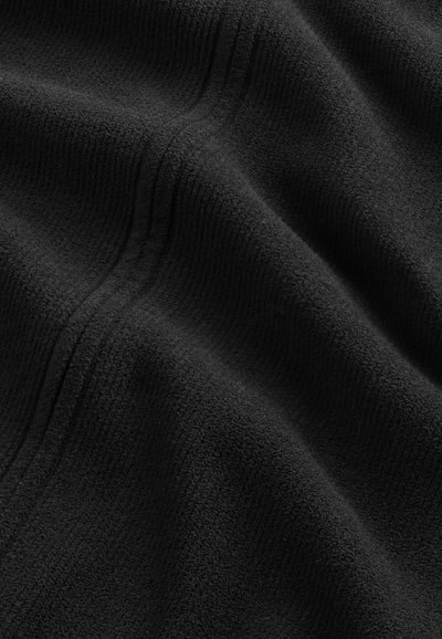 Tessuto in pile nero con superficie morbida e testurizzata e cuciture visibili che creano pieghe sottili.