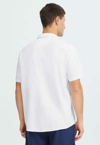 Chemise blanche à manches courtes en tissu léger et texturé avec un col classique et un ourlet incurvé, vue de dos.