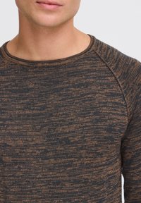 Schwarz-brauner gemusterter Pullover mit Rundhalsausschnitt, strukturiertem Stoff und Raglanärmeln. Nahaufnahme des Kragens und des Brustbereichs.