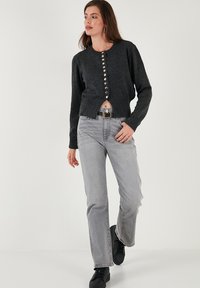 Gray knitted cardigan with metallic buttons, cropped design, and ribbed cuffs, paired with light gray straight jeans and black sneakers.