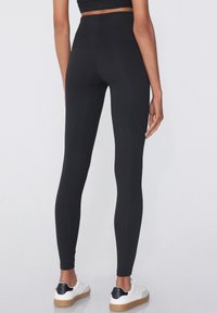 Leggings noirs taille haute avec une texture lisse, dotés d'un design ajusté et d'une taille sans couture, associés à des baskets blanches.
