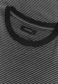 Close-up of a black and gray striped crew neck shirt with a black collar and a "Matinique" label inside the neckline.