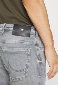 Grijze denim jeans hebben een achterzak met een zichtbare naad en een zwart leren label met de tekst "LTB" op de tailleband.