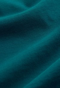 Zöldeskék színű kötött anyag finom bordás mintázattal és lágy redőkkel, amelyek puha árnyékokat és fényeket hoznak létre.