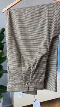 Brune og kremfargede rutete bukser laget av lett stoff, med rett snitt, mansjetter ved kanten og en hengelapp med størrelsesdetaljer.