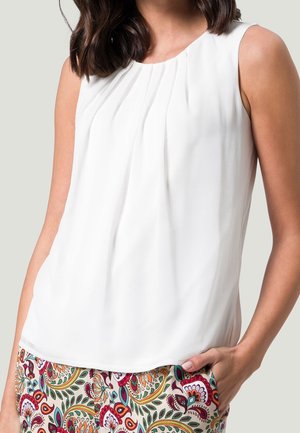 Hvid ærmeløs top med plisseret design ved halsudskæringen, kombineret med mønstrede bukser med farverige blomster-motiver og snoede blade.