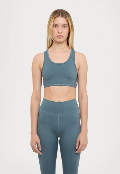Teal activewear set featuring a sports bra with wide straps and a logo band, paired with high-waisted leggings, both in a smooth, stretchy fabric.
