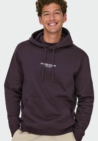 Hoodie violet foncé en tissu doux, avec une poche kangourou, une capuche à cordon et un texte blanc sur le devant.