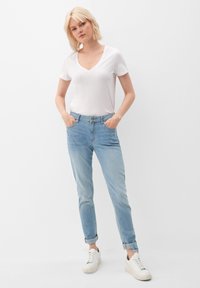 Camiseta blanca de cuello en v, jeans azul claro con puños enrollados y zapatillas blancas. Tejido de algodón, diseño ajustado, estilo casual, apariencia minimalista.