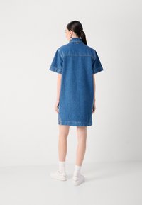Denim skjortekjole med korte ermer, krage, splitt på sidene og detaljer med ryggsøm. Lys blåfarge med en glatt tekstur.