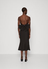 Schwarzes, trägerloses Midikleid mit einer großen Schleife auf der Rückseite, tailliertem Oberteil und ausgestellt Saum. Glattes Material und ein minimalistisches Design.