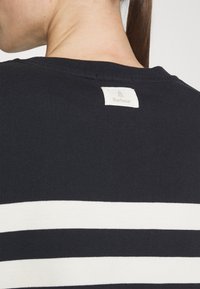 Bavlněné tričko v námořnické modři, s bílými vodorovnými pruhy a štítkem s logem "Barbour" na zadní straně. Hladká textura, design s kulatým výstřihem.