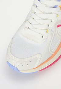 Adidas sportiv alb, fabricat din plasă și piele, cu șireturi plate albe și o talpă multi-colorată, cu accente de portocaliu, albastru și roz.