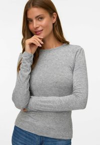Grijze longsleeve shirt gemaakt van zachte, gestructureerde stof, met een ronde hals en een fitted ontwerp. Draagt met blauwe denim jeans.