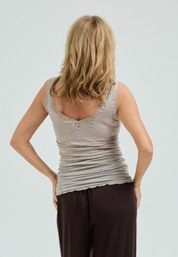 Graues Tanktop mit Spitzenbesatz, figurbetontem Design und weicher Textur. Kombiniert mit lockeren braunen Hosen, die einen lässigen Stil zeigen.