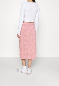 Avskuren vit långärmad topp med vågig nederkant, tillsammans med en rosa blommig midikjol. Vita canvas sneakers fullbordar outfiten.
