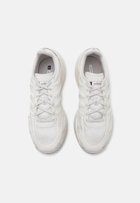 Hvite joggesko laget av mesh og syntetiske materialer, med en teksturert såle, snøring og minimal merkevare på tungen.