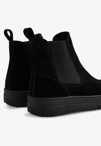 Bottines noires en suede avec des panneaux latéraux élastiques, des languettes de tirage, des semelles en caoutchouc texturé et un design élégant et profil bas.
