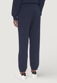 Granatowe spodnie dresowe z elastycznym pasem i mankietami, wykonane z miękkiego materiału, charakteryzujące się luźnym krojem i minimalną ilością przeszyć.