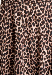 Potlač látky s leopardím vzorom, čierne a hnedé nepravidelné škvrny na béžovom pozadí, vrch látky zúžený so zreteľnými záhybmi.