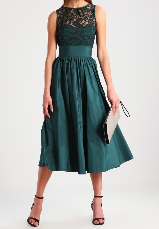 Türkisfarbenes Midi-Kleid mit Spitzenoverlay am Oberteil, schwingendem Rock und tailliertem Schnitt. Kombiniert mit einer Clutch und Riemchenabsätzen.