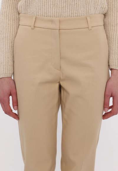 Beige, szabott nadrág sima textúrával, lapos elejű, övbújtatókkal és oldalsó zsebekkel. Finom varrás részletek az illeszkedések mentén.
