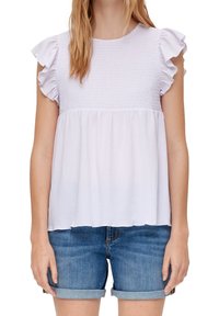 Kobieta w jasnofioletowej bluzce ze marszczonym karczkiem i falbankowymi krótkimi rękawkami, w niebieskich podwiniętych szortach dżinsowych, na białym tle.