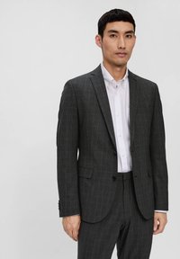 Szary, w kratkę garnitur o slim fit, z jednoprzylgowym żakietem, klapami w kształcie notcha i dwoma przednimi kieszeniami. Połączony z białą koszulą zapinaną na guziki.