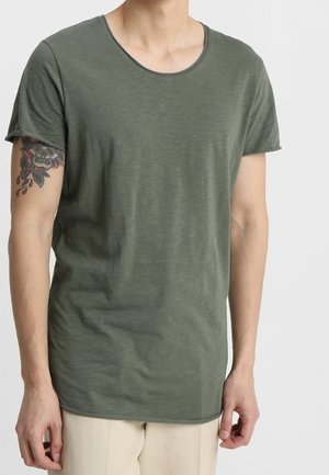 T-shirt vert olive à manches courtes en coton doux, doté d'un col rond et d'un ourlet arrière légèrement plus long. Texture lisse, coupe décontractée.