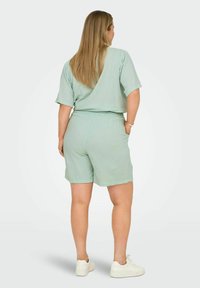 Světlý zelený dvoudílný outfit vyrobený z texturované látky, obsahující volný top s krátkým rukávem a kraťasy s elastickým pasem. Obsahuje kapsy na ruce.